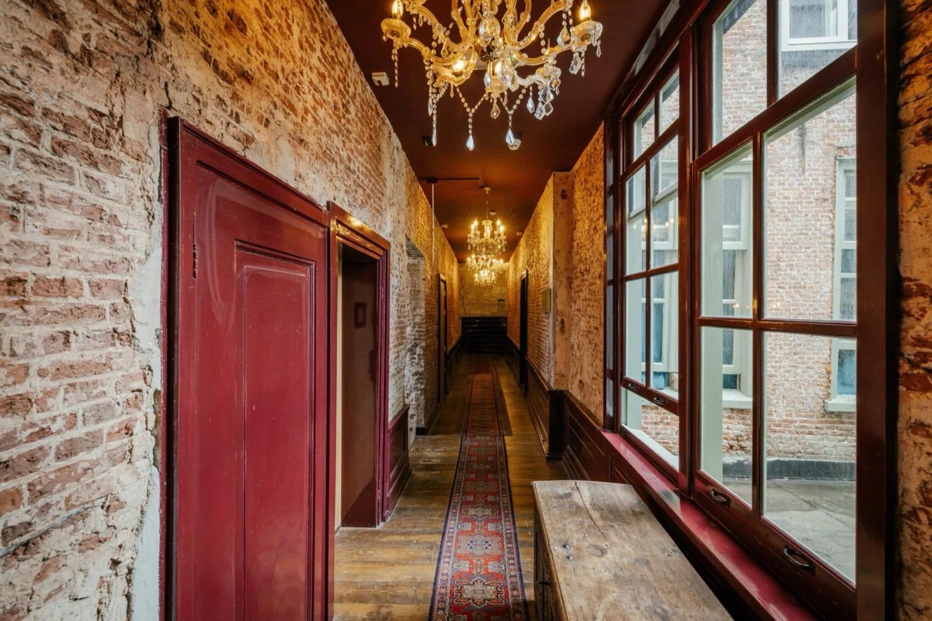 A corridor in Hotel 1635 in Haarlem, with exposed brickwork, red panelled doors and chandeliers