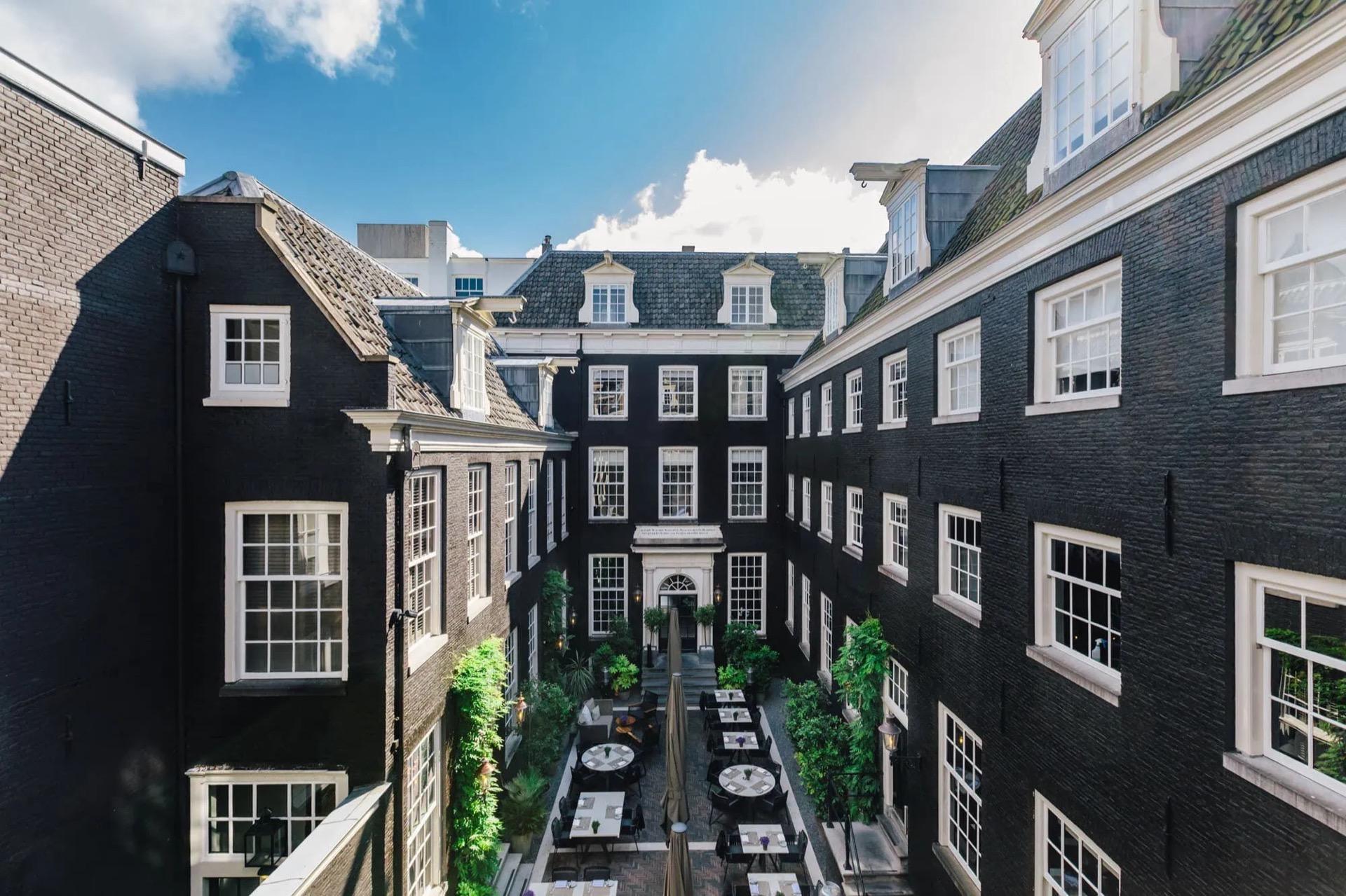 The inner courtyard of The Dylan Amsterdam, with laid tables between dark brick canal house facades