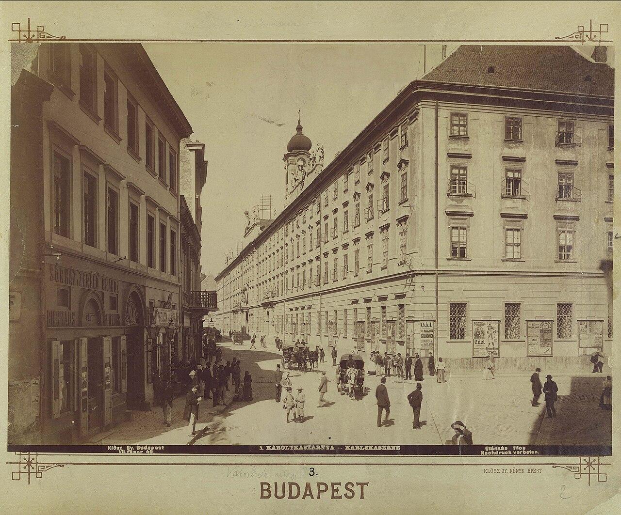 Black and white photograph of the long façade of the former Károly barracks, with horses and pedestrians in the street