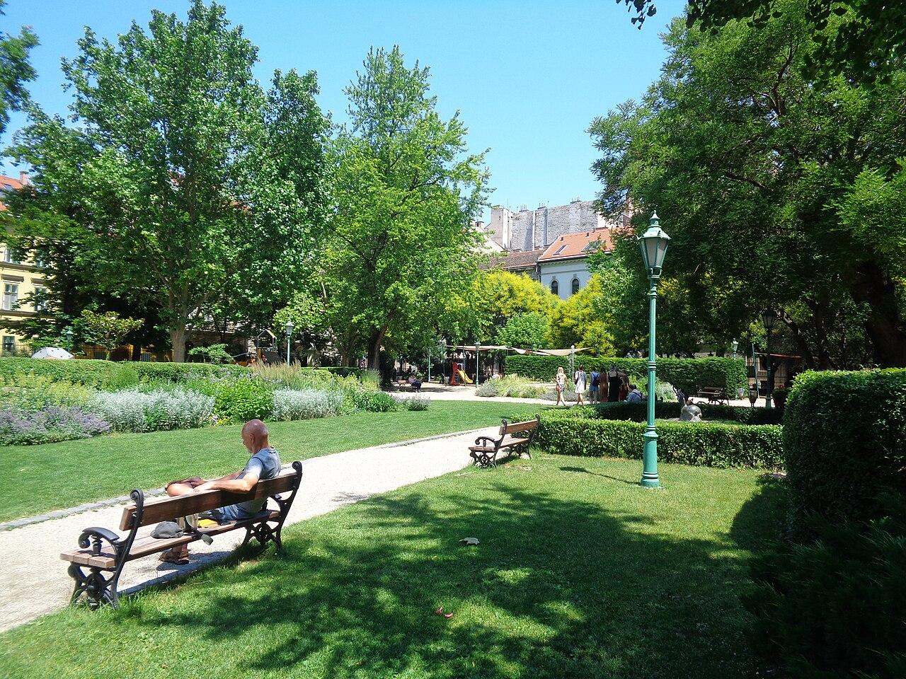 The garden on a summer day, with lawn, benches under the trees and gravel paths