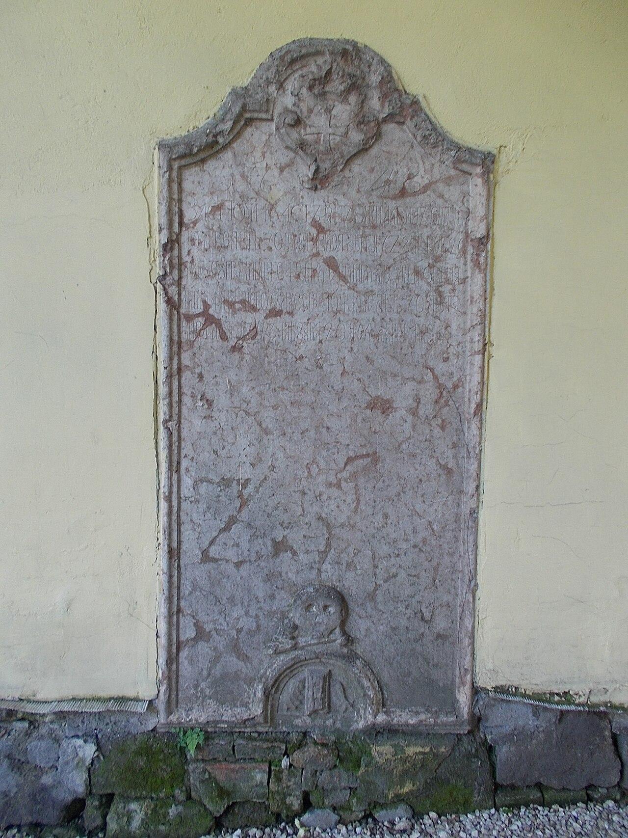 Old gravestone with carved lettering, standing upright against the garden wall